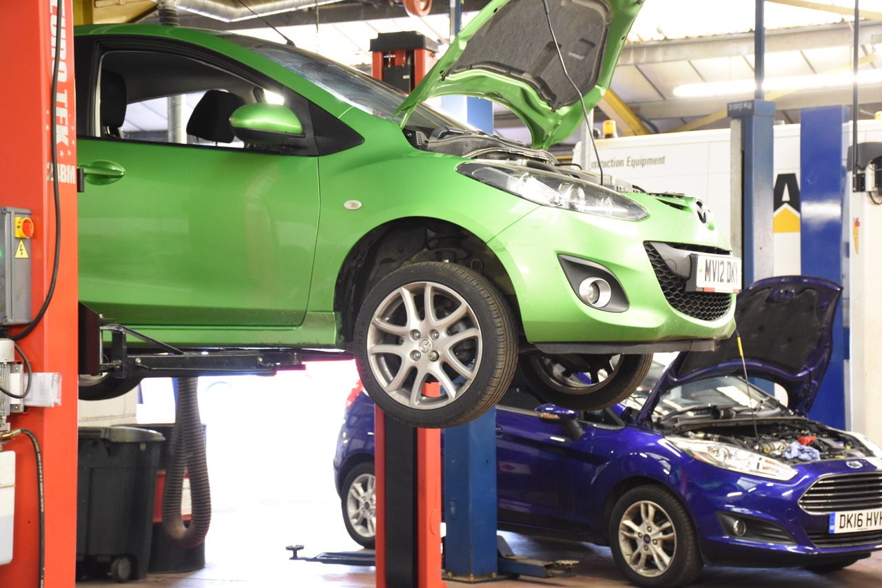 A green Mazda and a blue Ford Fiesta on lifts in the Buxton Car Centre workshop